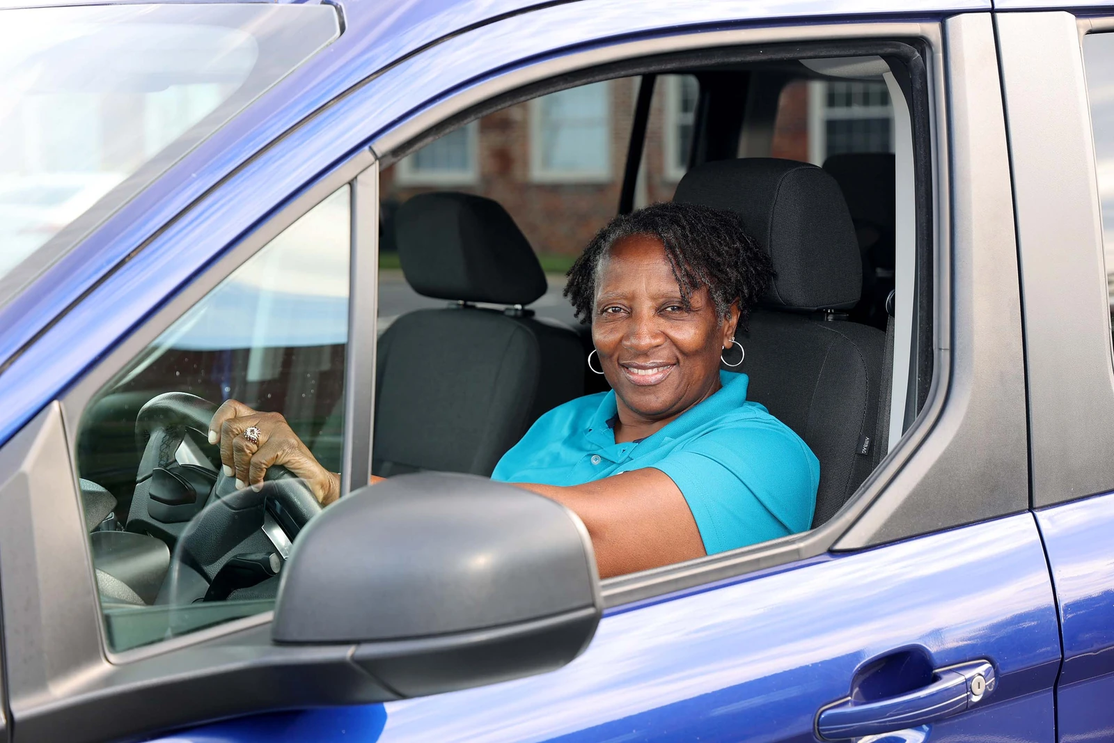 Lisa Bowden, owner and driver of Mimi's Express, smiling at the wheel of her blue METS van with the driver's window down