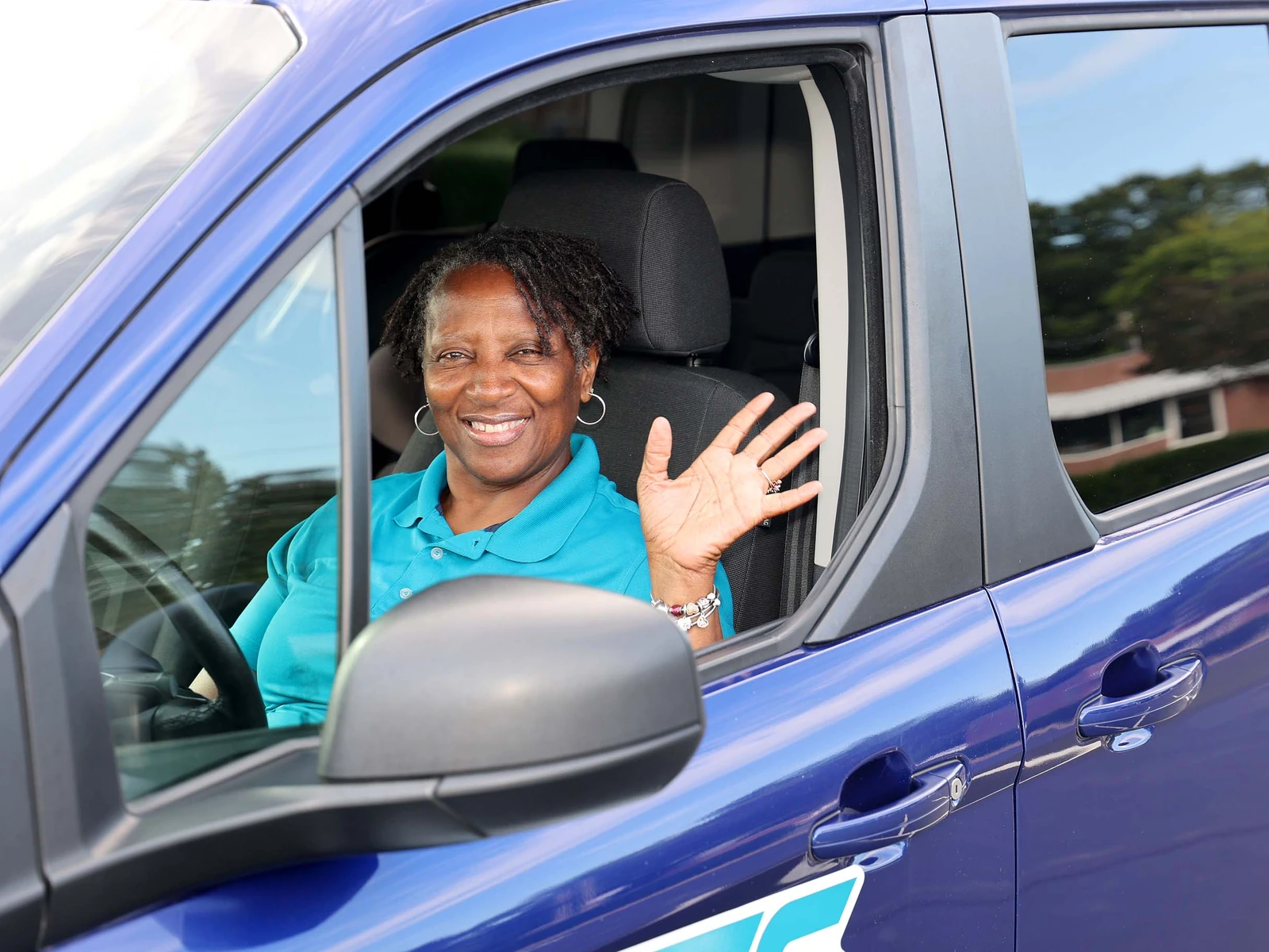 Lisa Bowden smiling and waving from the driver's window of her blue Mimi's Express van in Charlotte