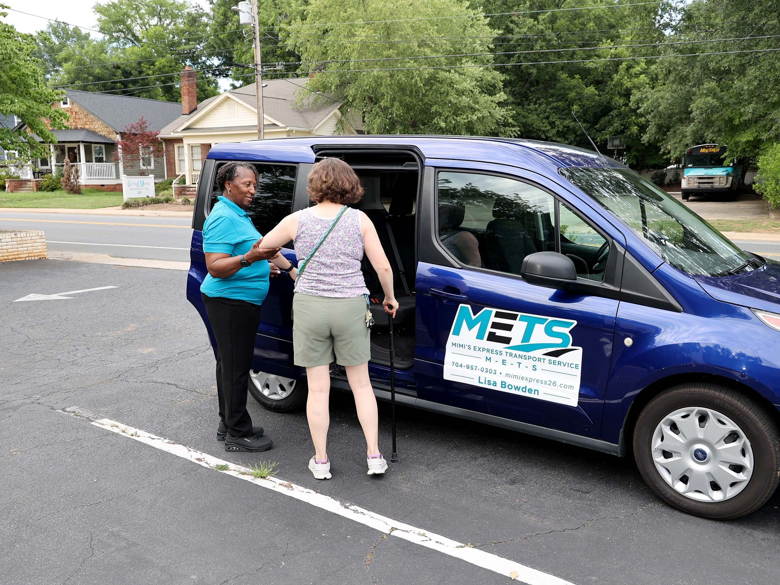 Lisa Bowden helping a senior rider using a cane step into the Mimi's Express van